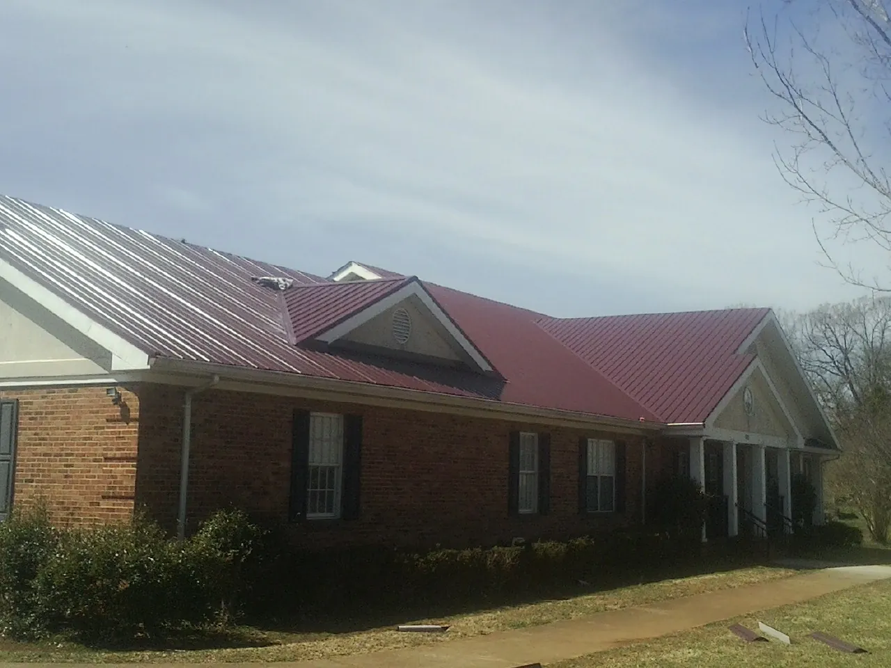 Red metal roof with gabled entries on a long brick building, from a Hail Damage Roof Repair job in Harwood