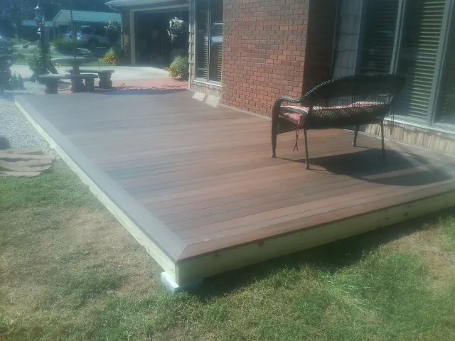 New wood deck and wicker chair beside a brick house in Harwood