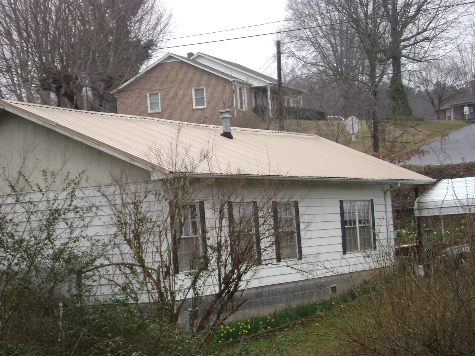 Tan metal roof on a white sided house set into a hillside — Commercial Roofing by Roofing Brothers in Harwood